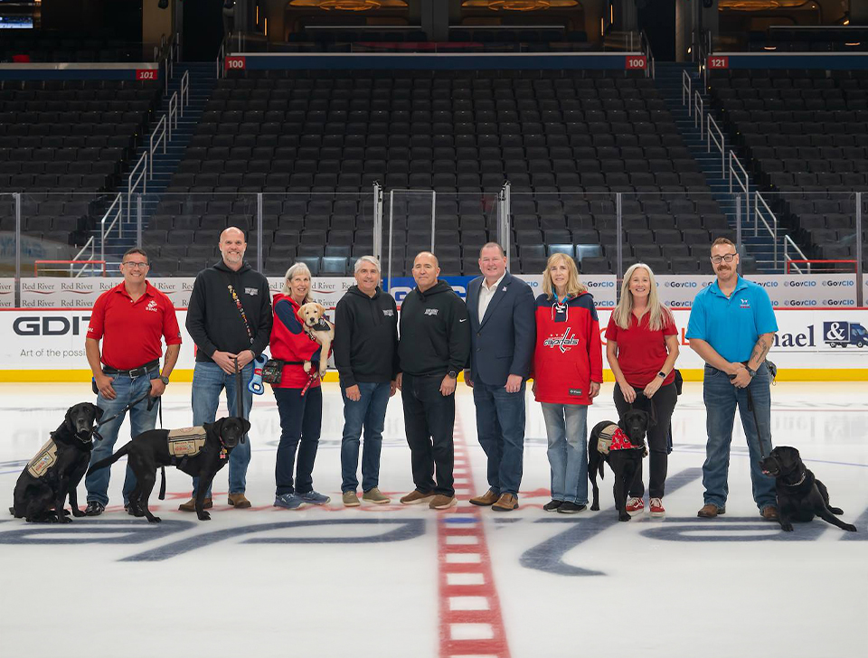 From left: Veteran Chris Sunday and Eddie, veteran and CACI employee Harley Brown with Claire, trainer Millie Jernigan holding CACI's first Good Dog - Bravo, President and CEO John Mengucci, CACI's Good Dogs Ambassador Mike Shields, America's VetDogs CEO John Miller, trainer Melissa Harrington, veteran Deana Stone with Gunner, and veteran Paul Sullivan with Sal.